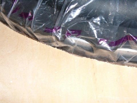 1997 Mercury Grand Marquis - Close-up of a black object wrapped in clear plastic packaging with purple printed markings, resting on a light tan carpeted surface, likely…