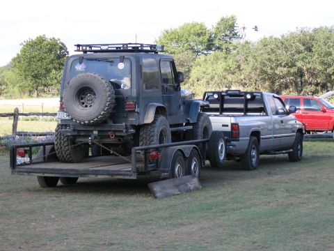 1996 Ford Bronco - A Jeep Wrangler is loaded onto a trailer pulled by a Dodge Ram pickup truck, with a red SUV visible in the background.