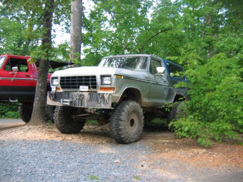 1992 Ford Mustang - A lifted 1978 Ford Bronco is parked off-road next to a red pickup truck, partially obscured by foliage.