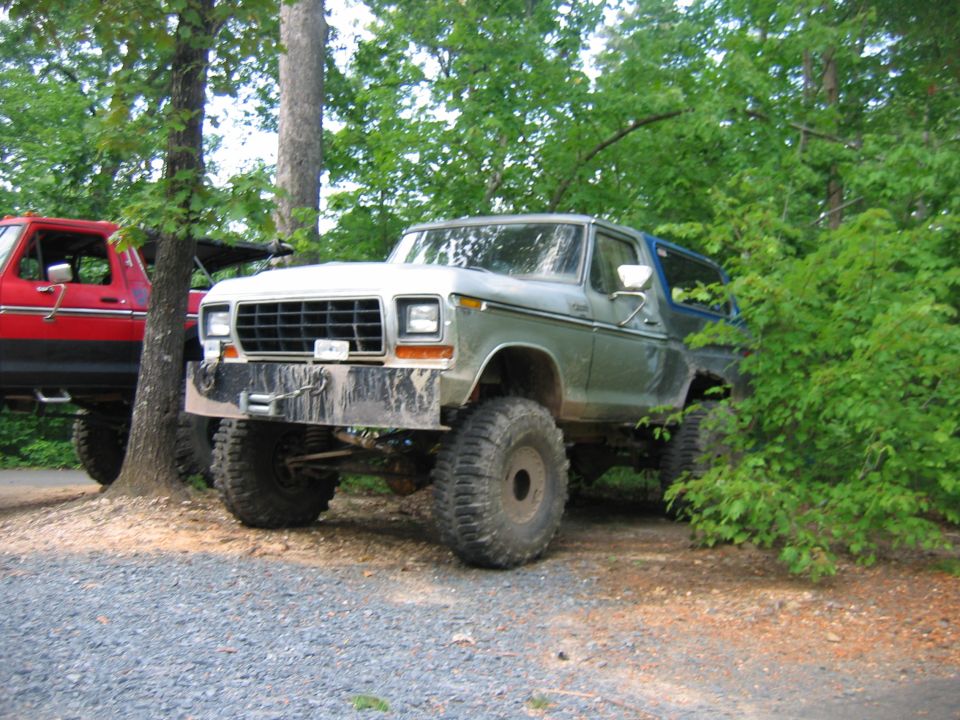 Lifted green Ford Bronco with big tires, parked next to a red truck