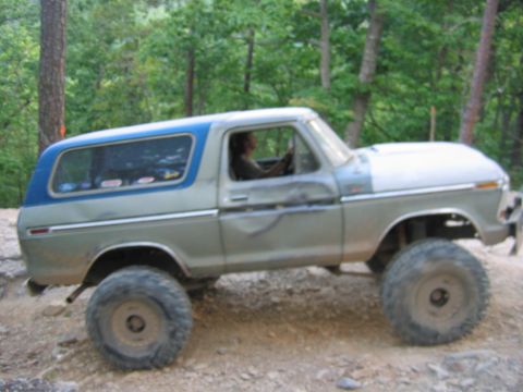 1992 Ford Mustang - A heavily modified Ford Bronco navigates an off-road trail with its driver visible.