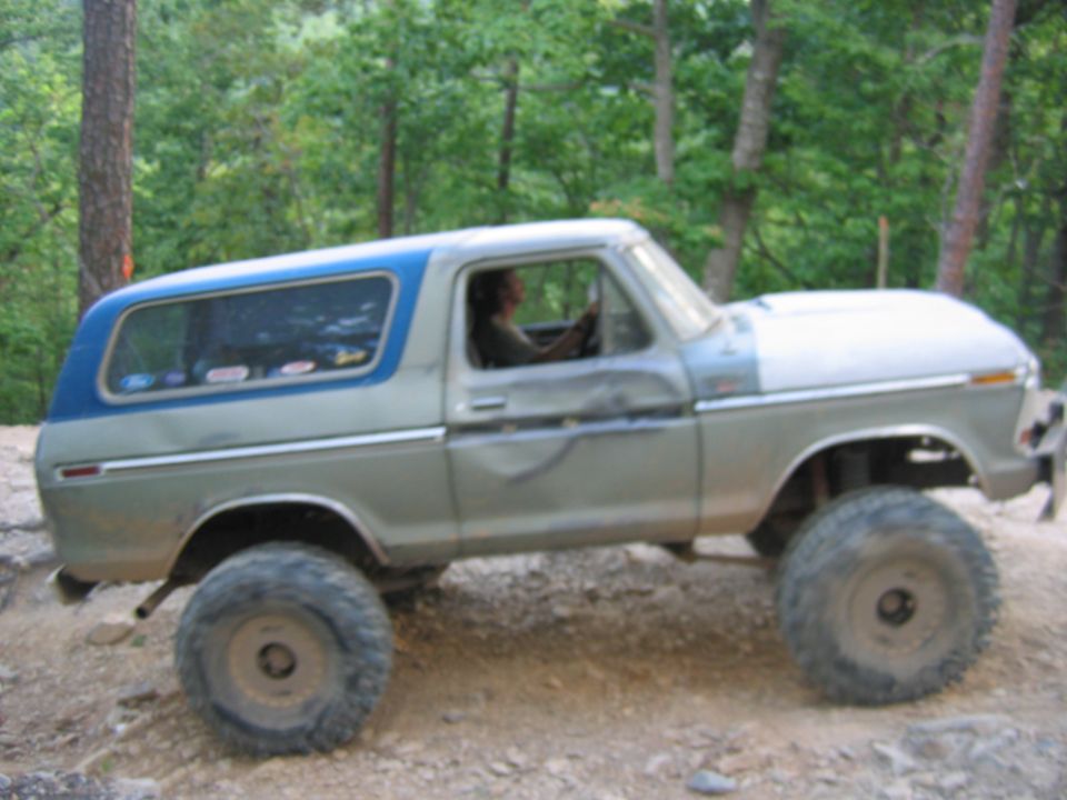 Modified Ford Bronco with large tires and blue roof, dented side panel, off-roading