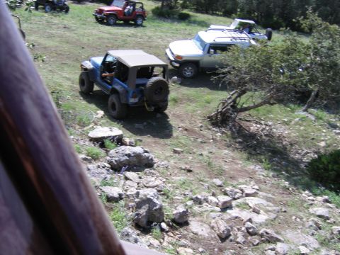 1996 Ford Bronco - Several off-road vehicles are parked on a rocky, grassy hillside under a bright sky.
