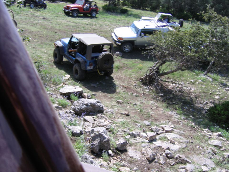Blue Jeep Wrangler with soft top and spare tire on rear, parked on a grassy hill