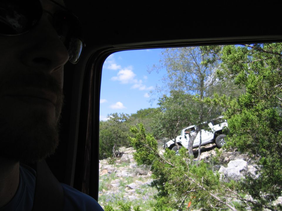 White SUV driving off-road on a hill with trees and rocks