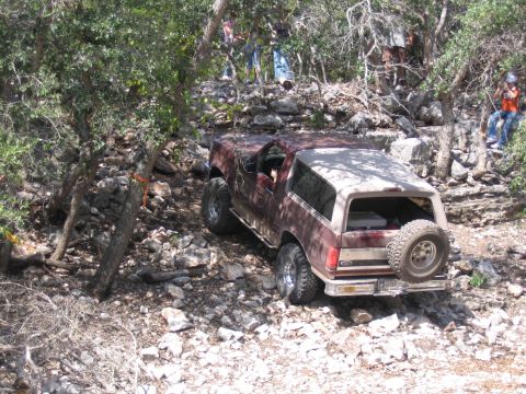 1996 Ford Bronco - 1996 Ford Bronco tackling a challenging off-road course in a wooded, rocky area.