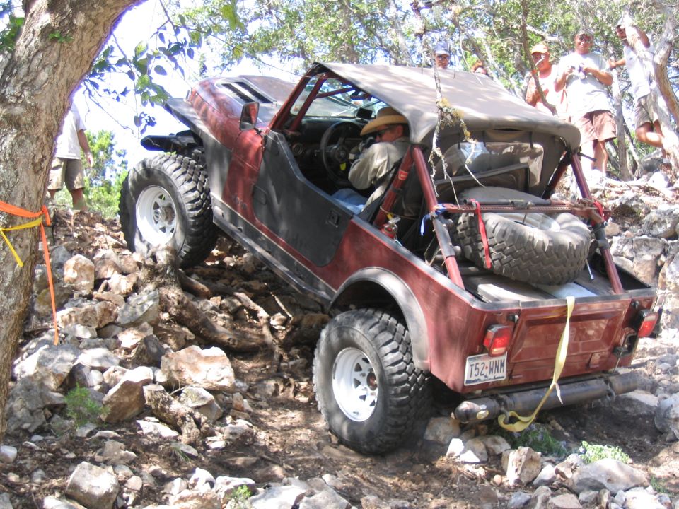 Red off-road vehicle with large tires navigating a rocky incline, driver wearing a hat