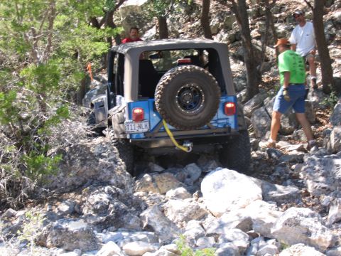 1996 Ford Bronco - A blue Jeep Wrangler TJ is seen maneuvering through a challenging rocky trail with several people observing.
