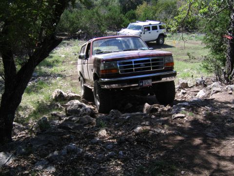 1996 Ford Bronco - A 1996 Ford Bronco navigates a rocky off-road trail, with another vehicle visible in the distance.