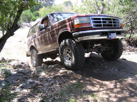1996 Ford Bronco - A maroon Ford Bronco navigates a rough, rocky terrain off-road.