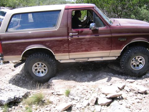 1996 Ford Bronco - A driver navigates a rocky trail in a maroon Ford Bronco with tan accents.