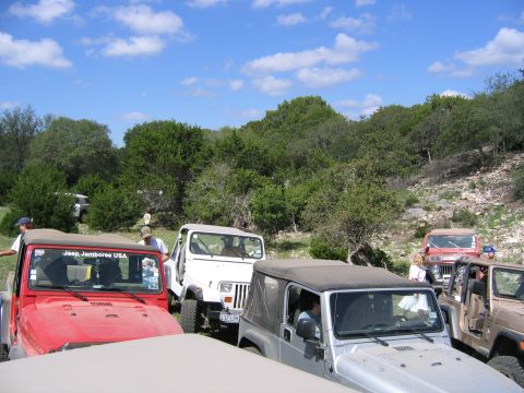 1996 Ford Bronco - A group of Jeeps are gathered in a natural setting under a partly cloudy sky.