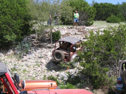 1996 Ford Bronco - Several Jeeps navigate a challenging off-road trail with rocky terrain and dense vegetation.