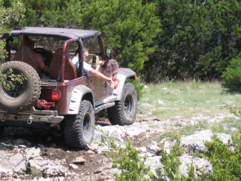 1996 Ford Bronco - A red Jeep Wrangler navigates a rocky trail surrounded by trees.