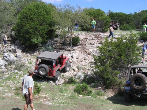 1996 Ford Bronco - Several Jeeps are seen off-roading on a rocky hill with trees and brush.