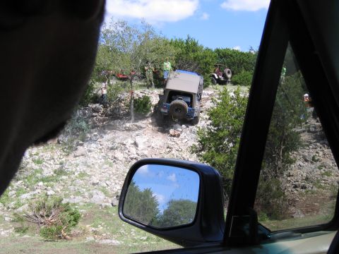 1996 Ford Bronco - Multiple off-road vehicles navigate a steep, rocky terrain under a partly cloudy sky.