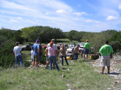 1996 Ford Bronco - People gathered around multiple off-road vehicles in a rural setting under a partly cloudy sky.