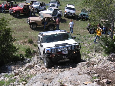 1996 Ford Bronco - A white Hummer H2 tackles a challenging rocky trail, with a convoy of other off-road vehicles visible in the distance.