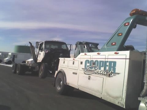 1992 Ford Bronco - A tow truck is seen towing a semi-truck chassis on a road under a cloudy sky.