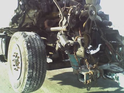 1992 Ford Bronco - The front tire and engine of a heavily damaged vehicle are visible, with chains attached to the frame.