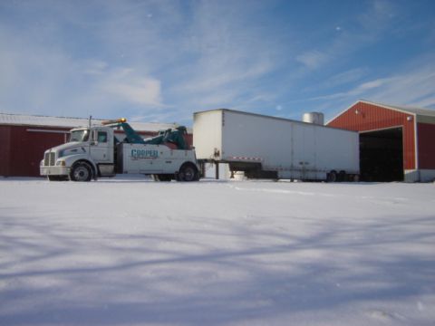 1992 Ford Bronco - A tow truck and trailer are parked in a snowy landscape next to red buildings.