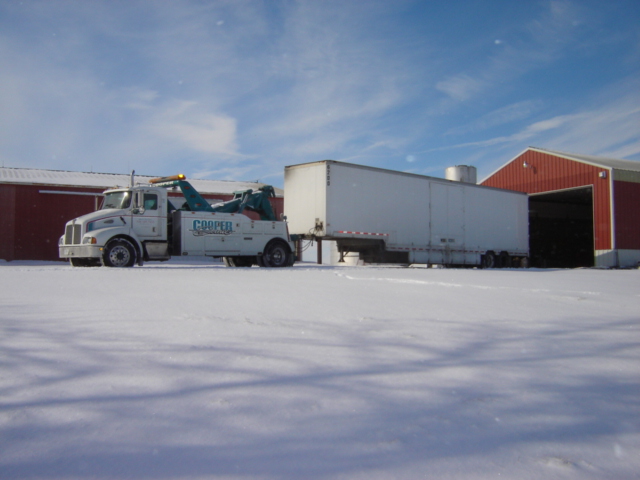 White tow truck with 'Cooper' logo pulling a white semi-trailer in the snow