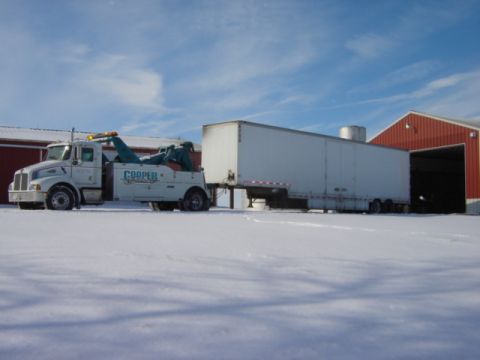 1992 Ford Bronco - A tow truck is parked in the snow, connected to a large white trailer.