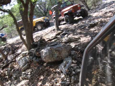 1996 Ford Bronco - Several off-road vehicles navigate a challenging, rocky terrain surrounded by trees.