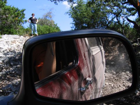 1996 Ford Bronco - Reflection in the side mirror shows the side of a red SUV with a person inside, driving on a rocky trail.