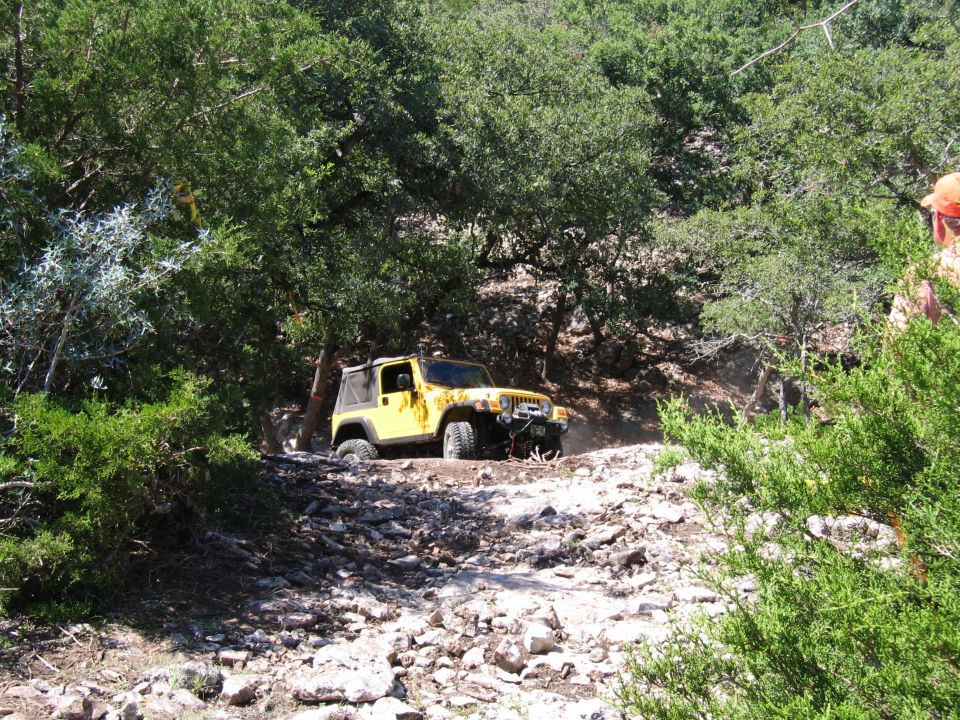 Yellow Jeep Wrangler driving on a rocky, wooded trail