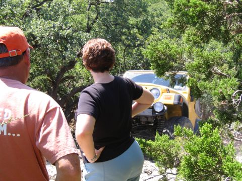 1996 Ford Bronco - Two people observe a yellow Jeep Wrangler navigating a wooded trail.