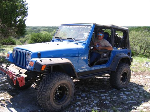 1996 Ford Bronco - A blue Jeep Wrangler is parked on a rocky trail with a driver inside and a scenic background.