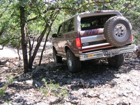 1996 Ford Bronco - A 1996 Ford Bronco navigates a rocky, wooded path with its spare tire mounted externally.