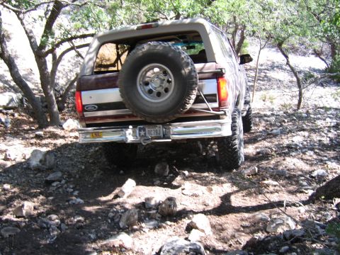 1996 Ford Bronco - The rear view of a brown Ford Bronco navigating a rocky, wooded trail.