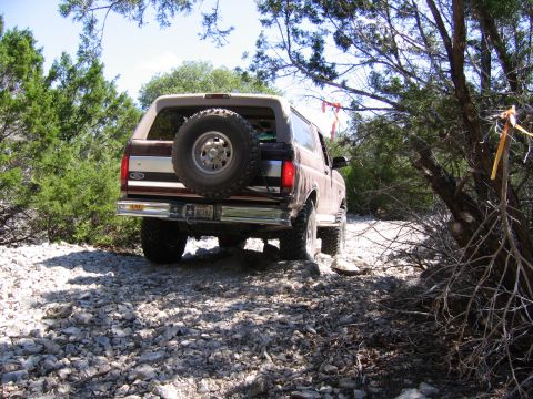 1996 Ford Bronco - 1996 Ford Bronco navigating a rough, rocky terrain with trees and brush surrounding the path.
