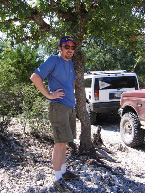 1996 Ford Bronco - A man stands by a tree, with a maroon 1992 Ford F-150 and a white SUV parked behind him.