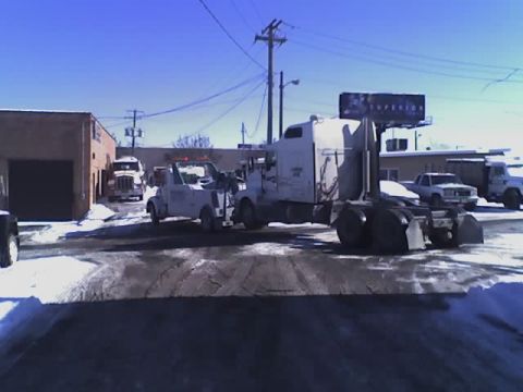 1992 Ford Bronco - Multiple tow trucks and semi-trucks are visible in a snowy industrial area under a clear blue sky.