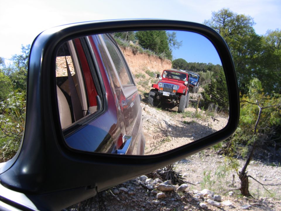 Red Jeep Wrangler on a dirt road, reflected in a side mirror