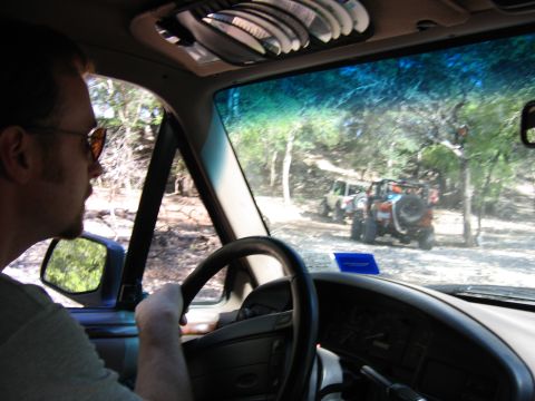 1996 Ford Bronco - A driver's perspective from inside an SUV as they navigate a dirt road, with other off-road vehicles visible ahead.