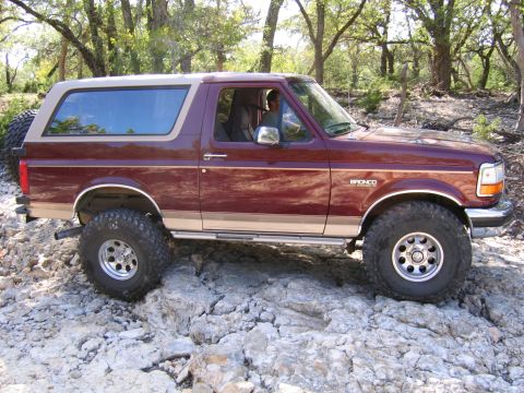 1996 Ford Bronco - A maroon Ford Bronco with a tan removable top navigates a rocky trail.