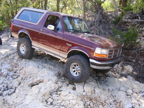 1996 Ford Bronco - A maroon 1996 Ford Bronco navigates a rocky trail with its tan removable top in place.