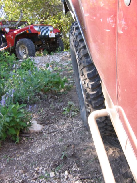 1996 Ford Bronco - Two off-road vehicles on a rocky trail with vegetation.