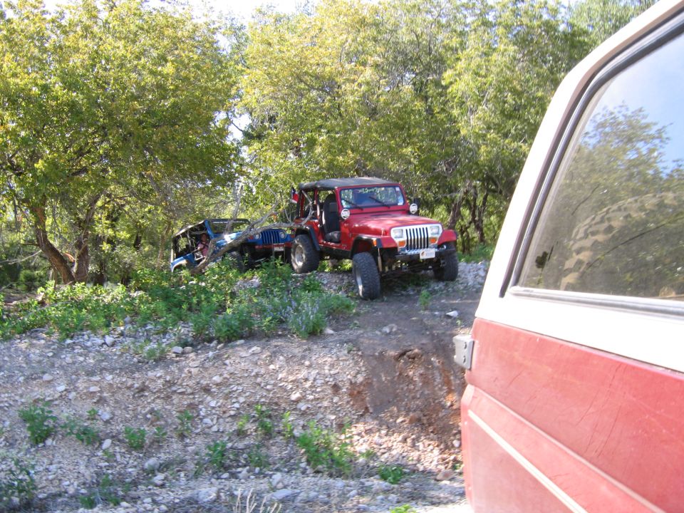 Red Jeep Wrangler parked on a dirt path next to a blue Jeep Wrangler on its side