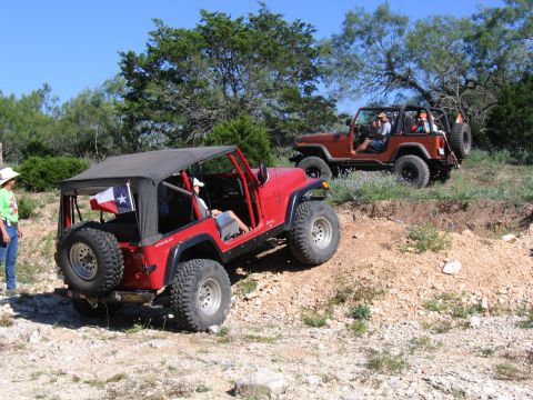 1996 Ford Bronco - Two Jeep Wranglers navigate a dirt trail with sparse vegetation under a clear blue sky.