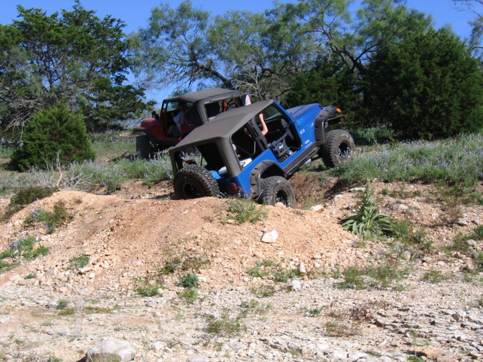 Blue Jeep partially in a ditch with red Jeep behind it on a dirt trail