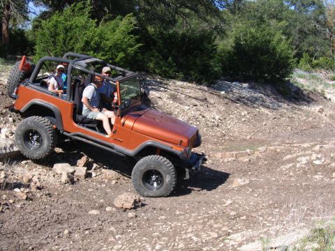 1996 Ford Bronco - A group enjoys an off-road adventure in an orange Jeep Wrangler navigating a challenging, rocky terrain.
