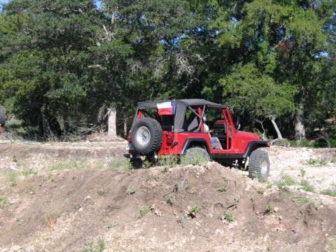 1996 Ford Bronco - A red Jeep Wrangler navigates a dirt path surrounded by trees.