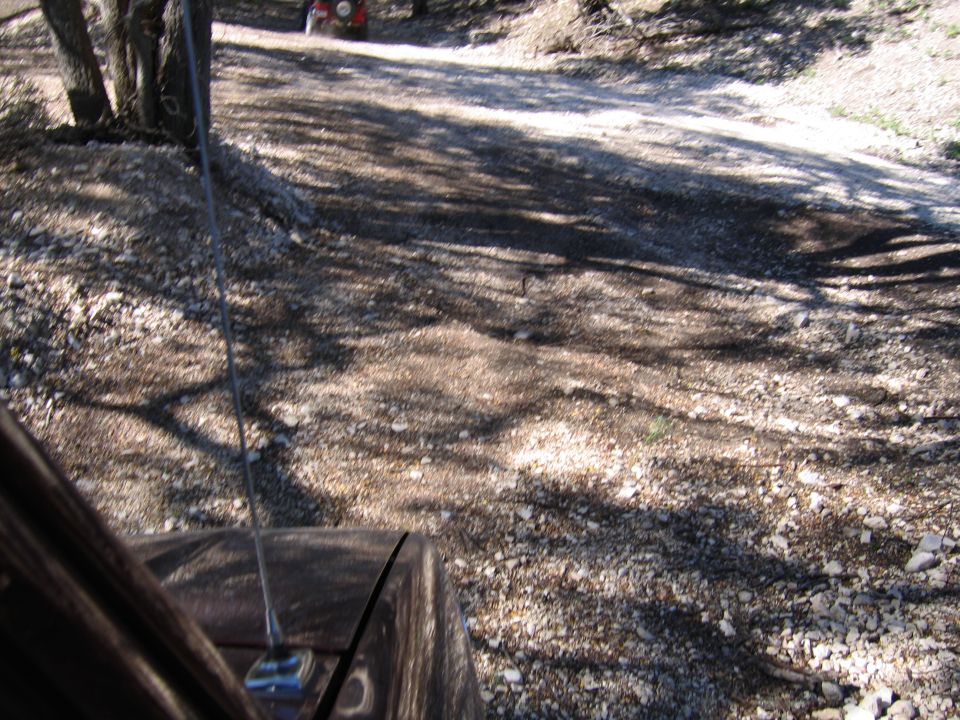 View from inside a vehicle looking at a dirt road with trees and a red ATV in the distance