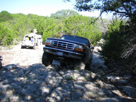 1996 Ford Bronco - A 1996 Ford Bronco tackles a challenging rocky path, with another vehicle visible on the trail ahead.