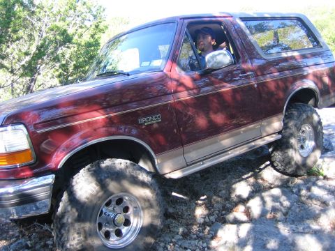 1996 Ford Bronco - A man drives a maroon Ford Bronco over rocks on a sunny day.